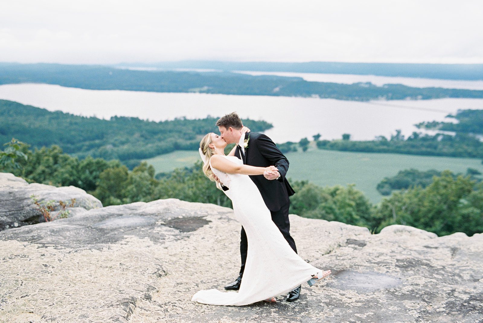 Bride and groom dip for a kiss on the rocky bluff at Infinity Event Venue in Section Alabama