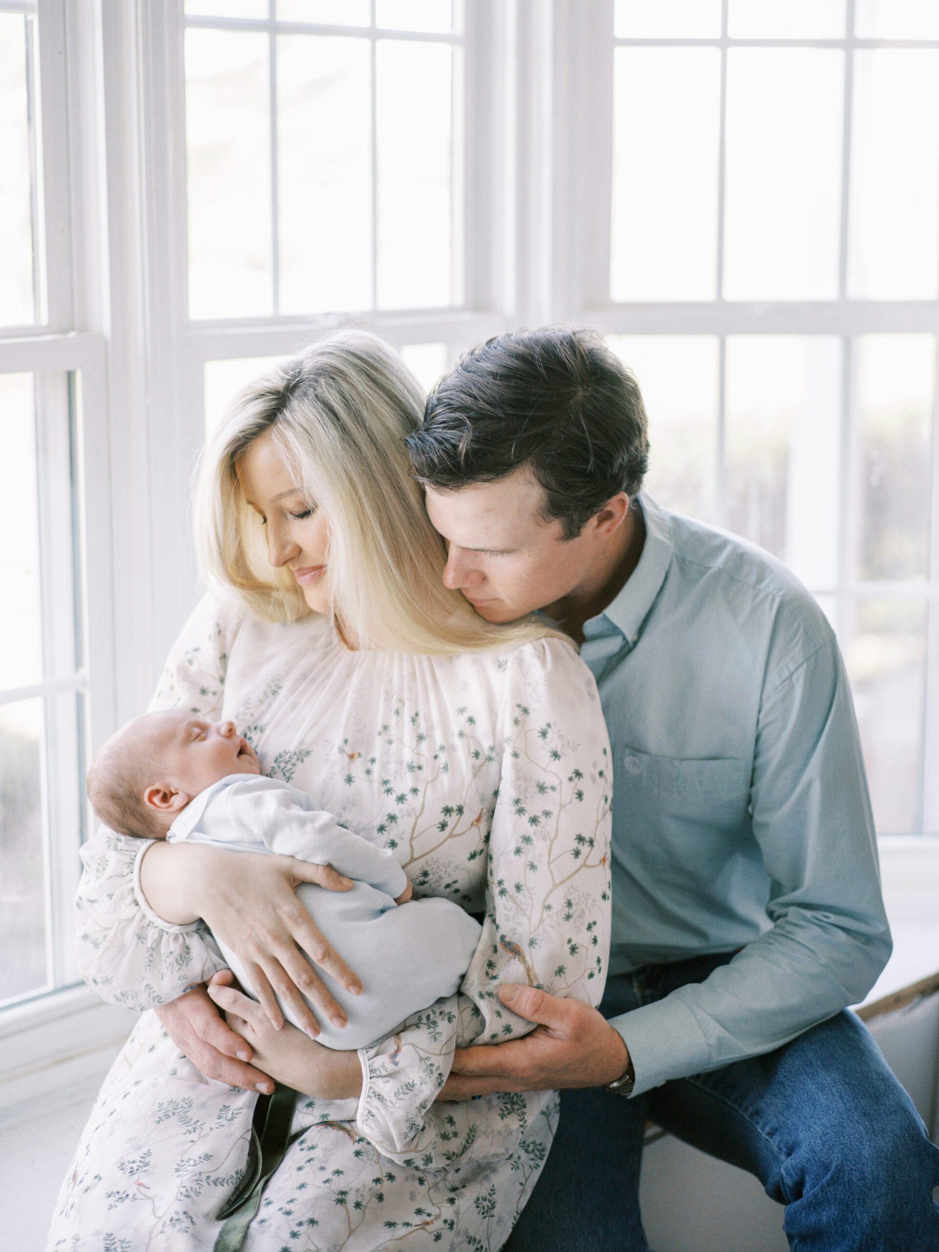newborn baby boy and parents in front of window wrapped in light